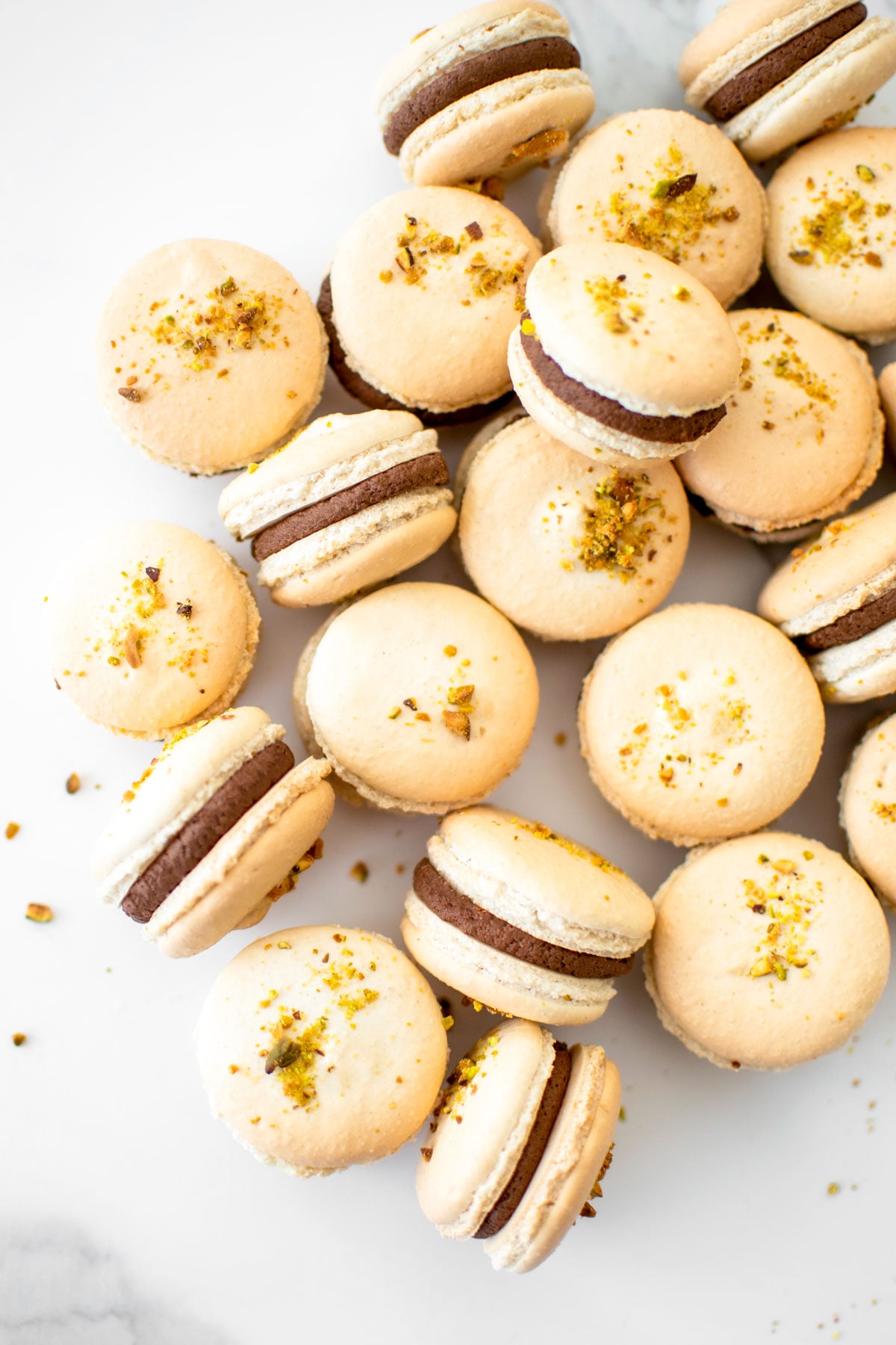 chocolate pistachio french macarons on a marble counter.
