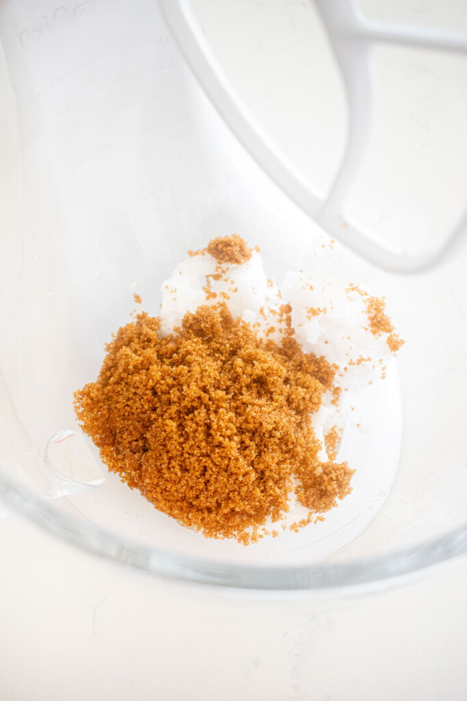 coconut oil and sugar in a glass mixing bowl on a marble counter.