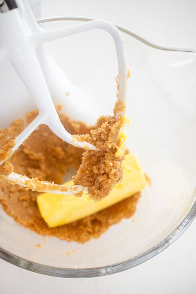 creamed butter and coconut oil in a glass mixing bowl with a stick of butter on a marble counter.