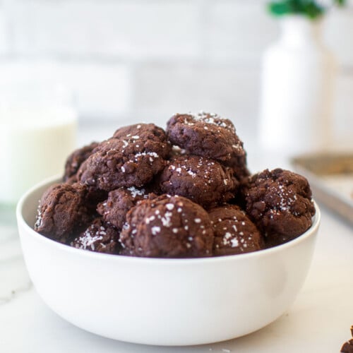 bowl of chocolate sea salt mini cookies on a marble counter with a glass of milk.