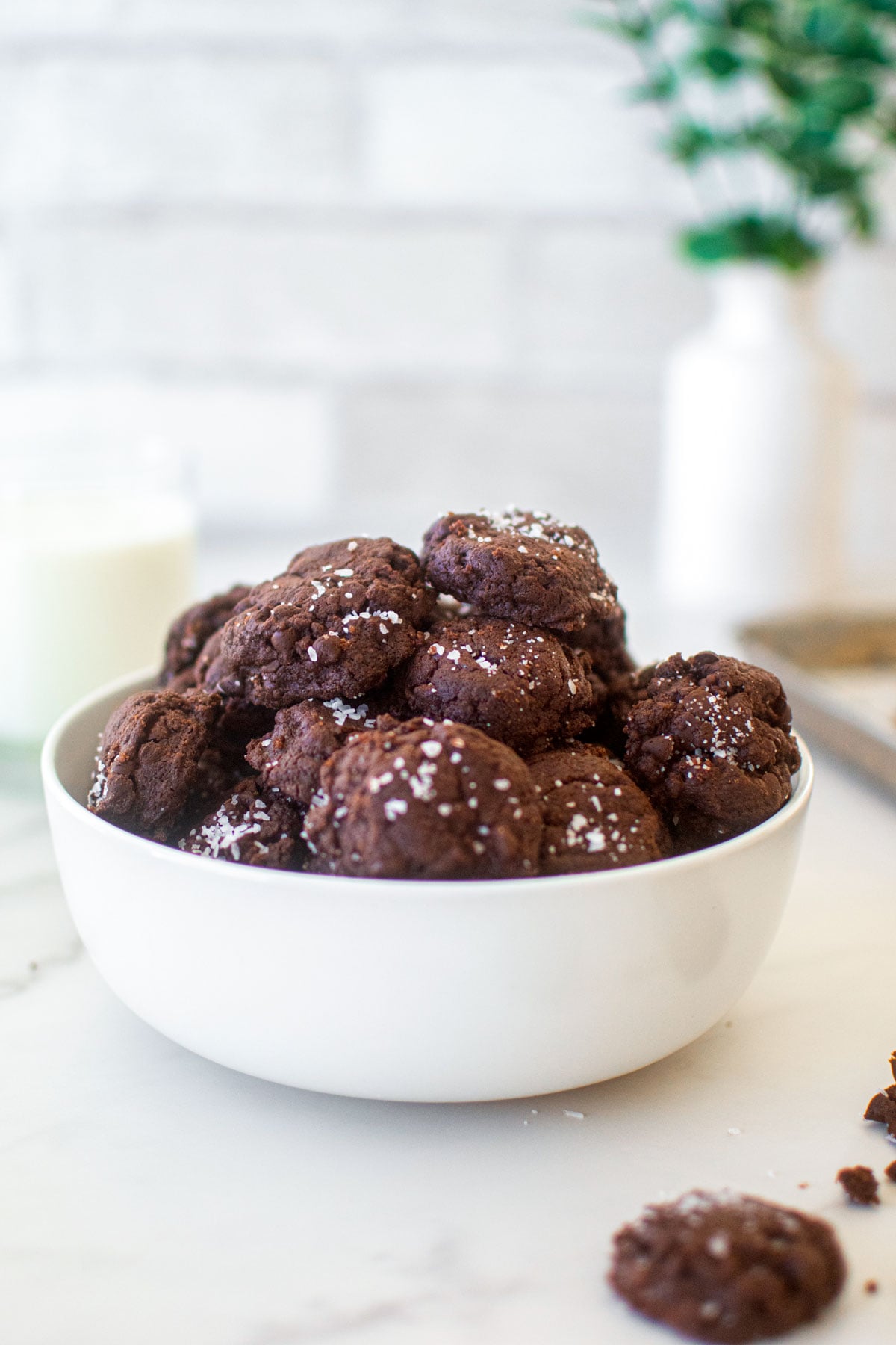 bowl of chocolate sea salt mini cookies on a marble counter with a glass of milk.