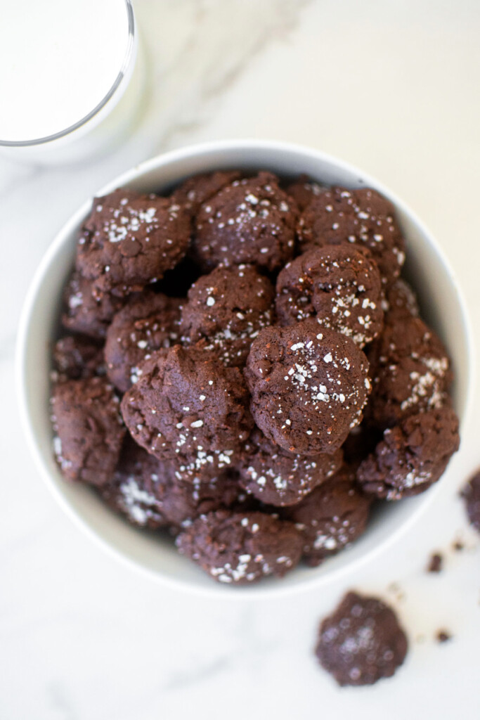 bowl of chocolate sea salt mini cookies on a marble counter with a glass of milk.