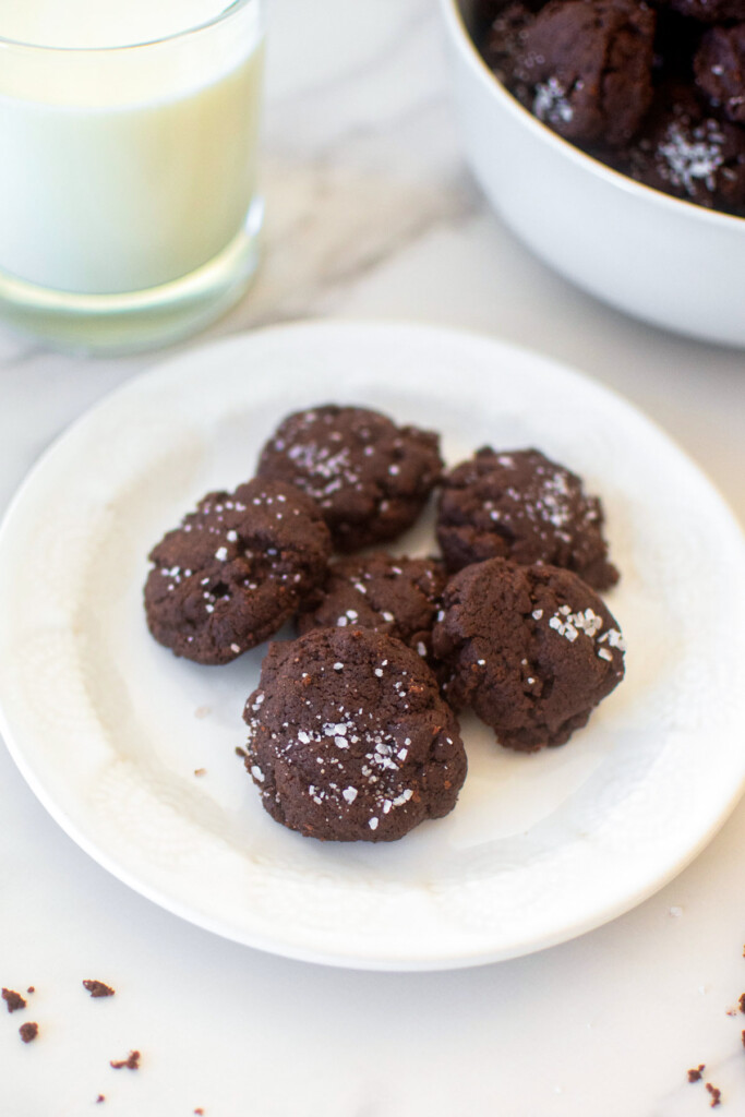 plate of chocolate sea salt mini cookies on a marble counter with a glass of milk.