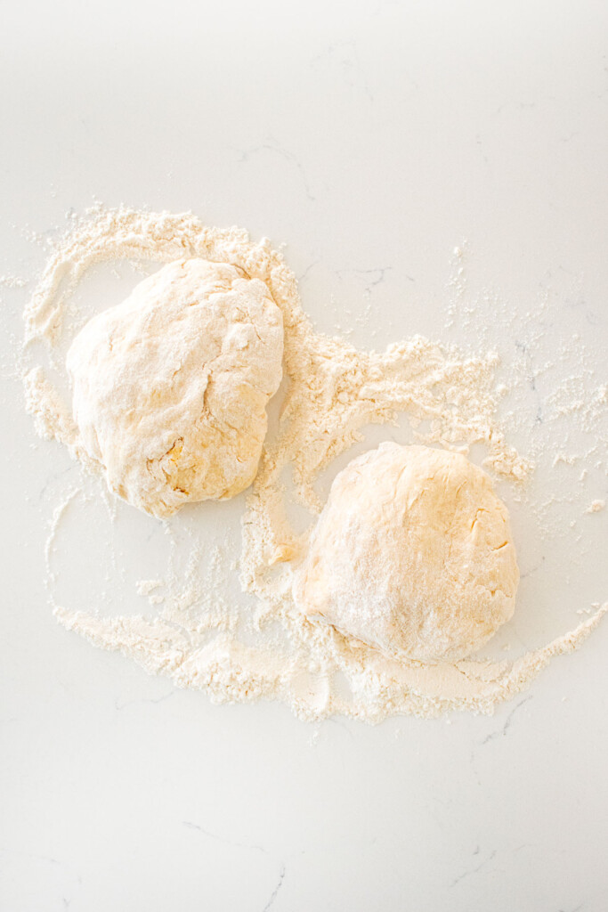 two pizza doughs on a white marble counter with flour.