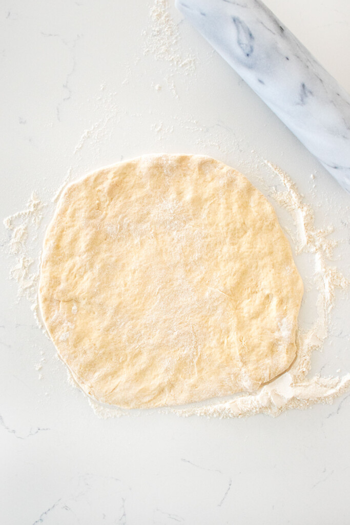 pizza dough rolled out on a white marble countertop.