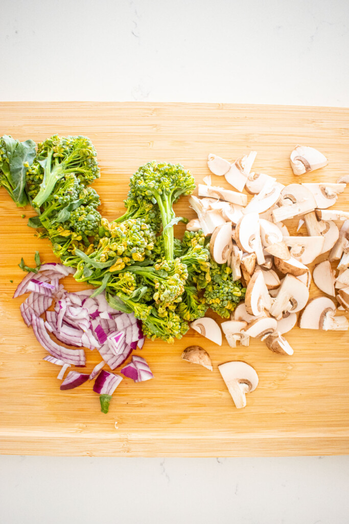 chopped pizza toppings on a bamboo cutting board on a white marble counter.