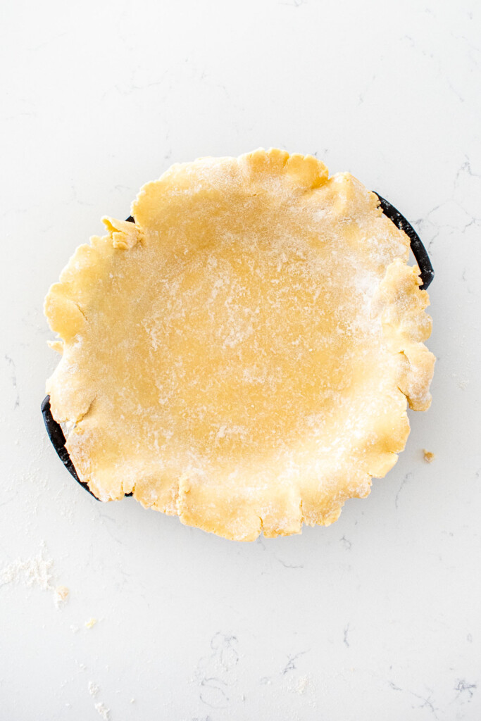 pie crust in a cast iron pie pan on a white marble counter.