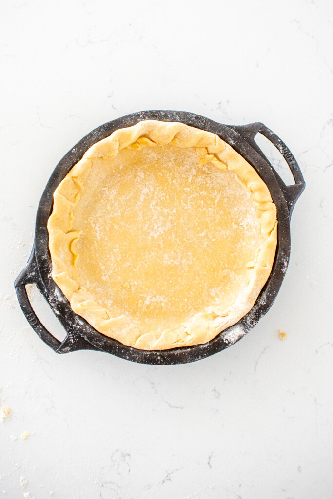 pie crust with edges folded into the pan in a cast iron pie pan on a white marble counter.