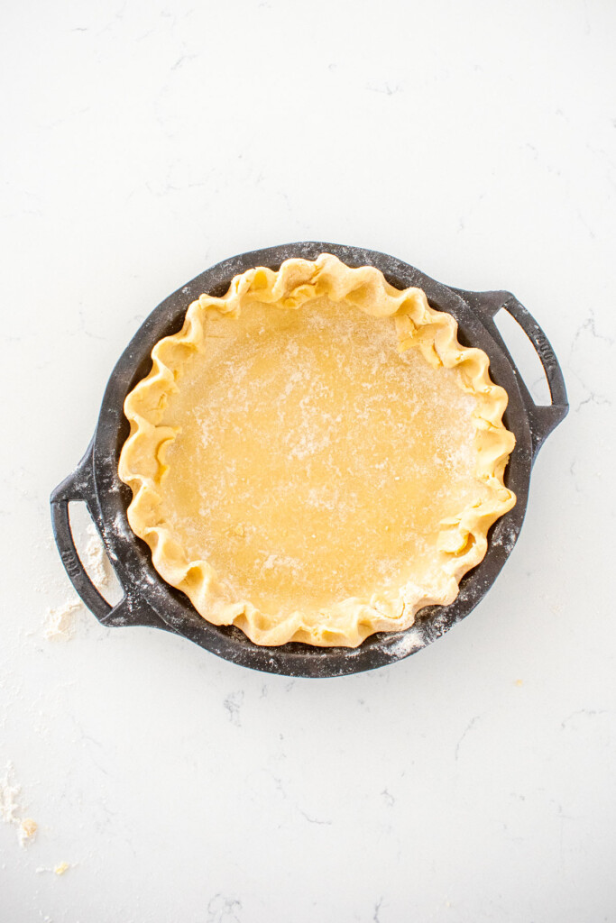 pie crust with fluted curst in a cast iron pie pan on a white marble counter.