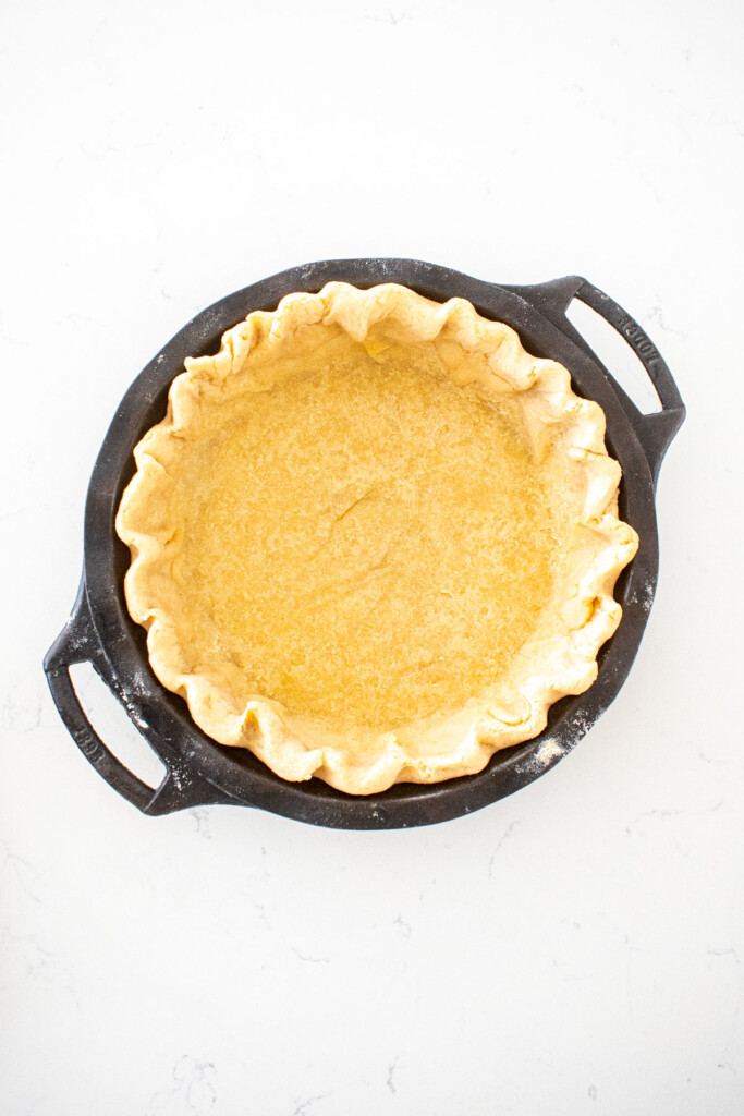 par baked pie crust in a cast iron pie pan on a white marble counter.