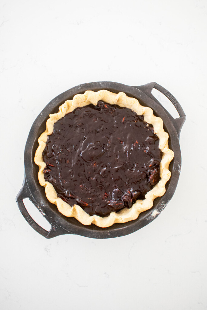 chocolate bourbon pecan pie filling in a par baked pie crust on a white marble counter.