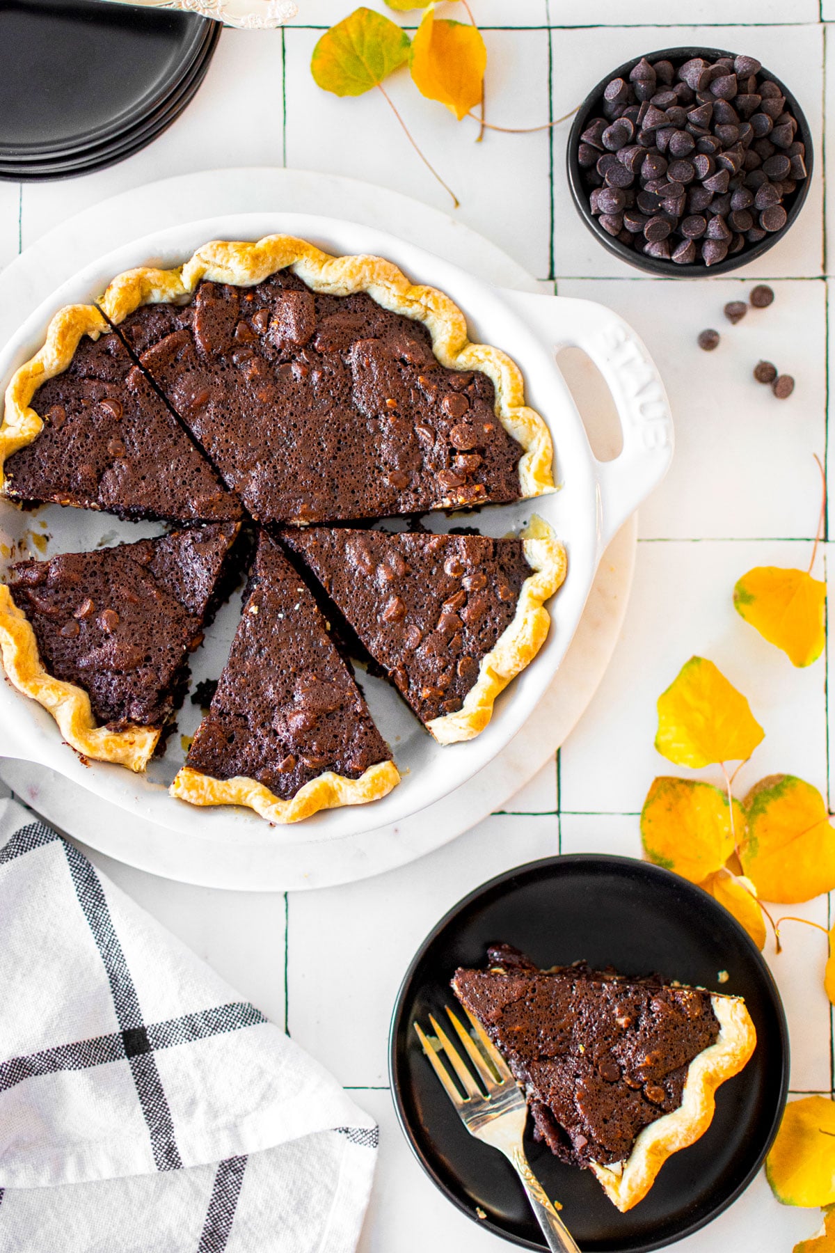 chocolate bourbon pecan pie cut into slices in a white pie dish on a white tile countertop.