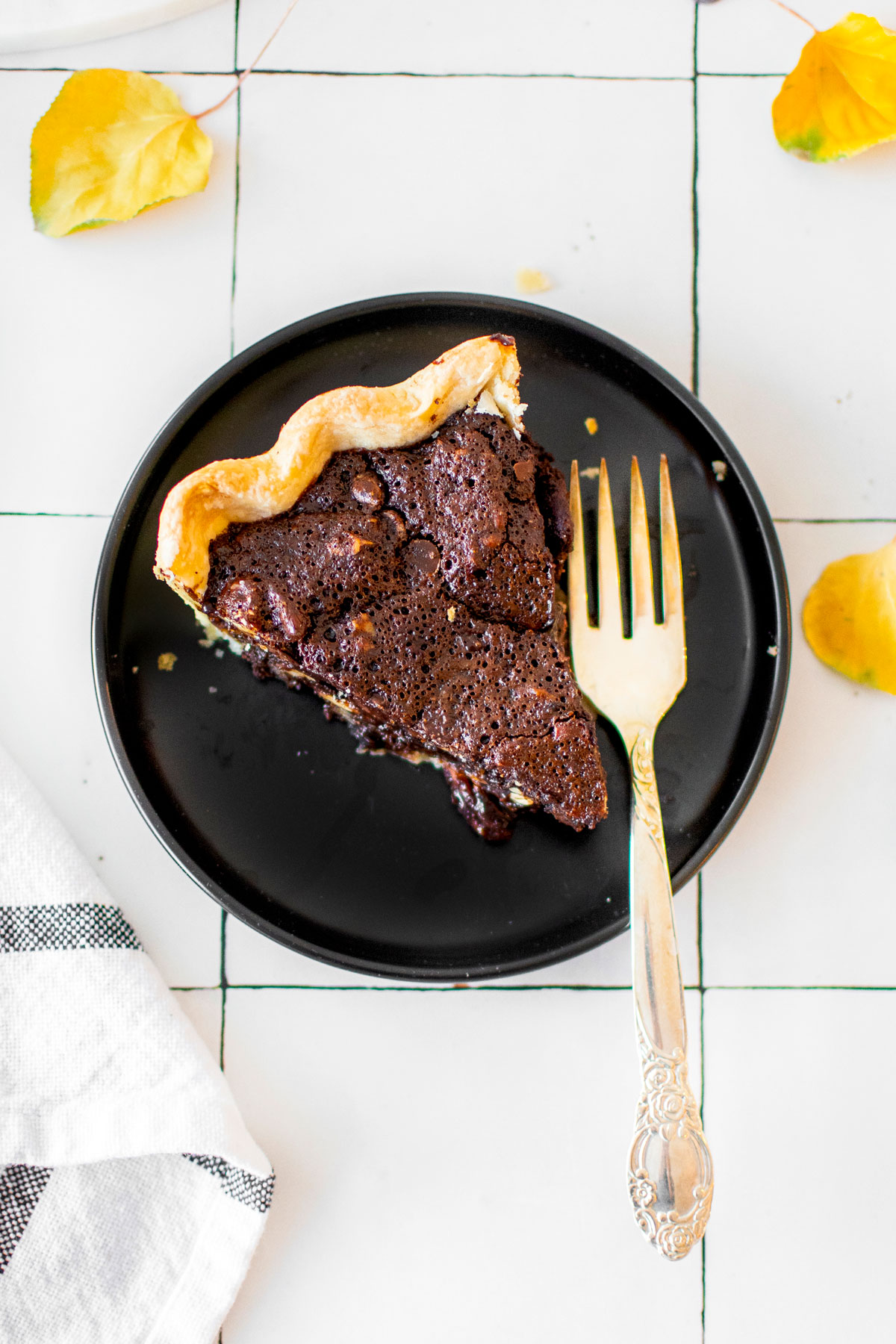 slice of chocolate bourbon pecan pie on a black plate on a white tile countertop.
