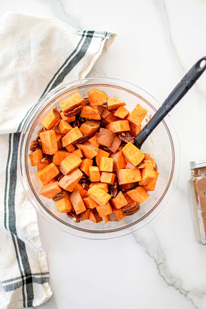 cinnamon sweet potatoes and pecans in a glass mixing bowl on a marble countertop.