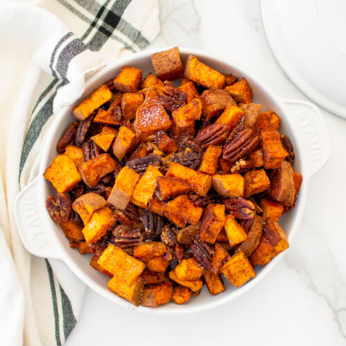 roasted cinnamon sweet potatoes with pecans in a serving dish on a marble countertop.