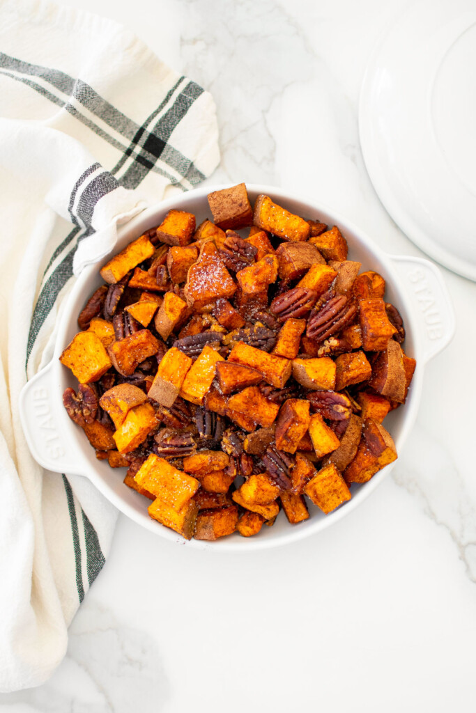 roasted cinnamon sweet potatoes with pecans in a serving dish on a marble countertop.