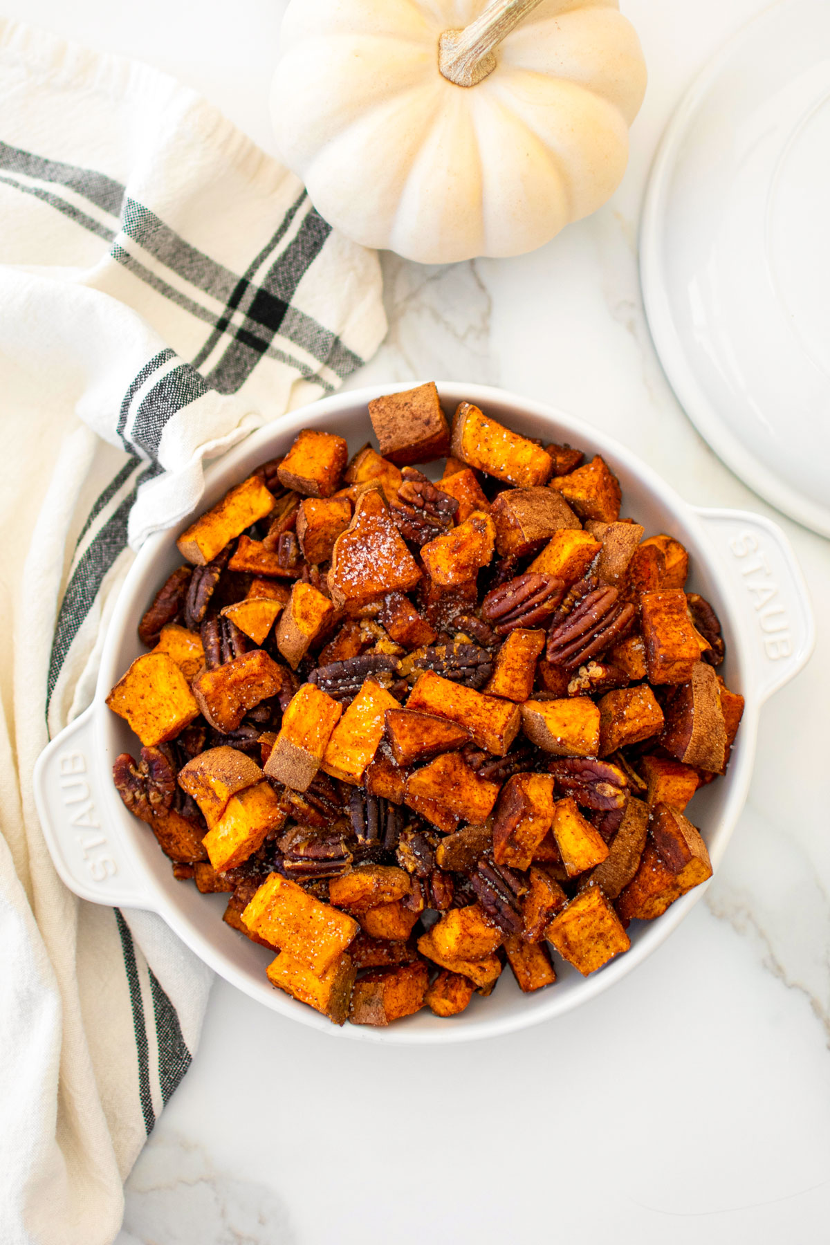 roasted cinnamon sweet potatoes with pecans in a serving dish on a marble countertop.