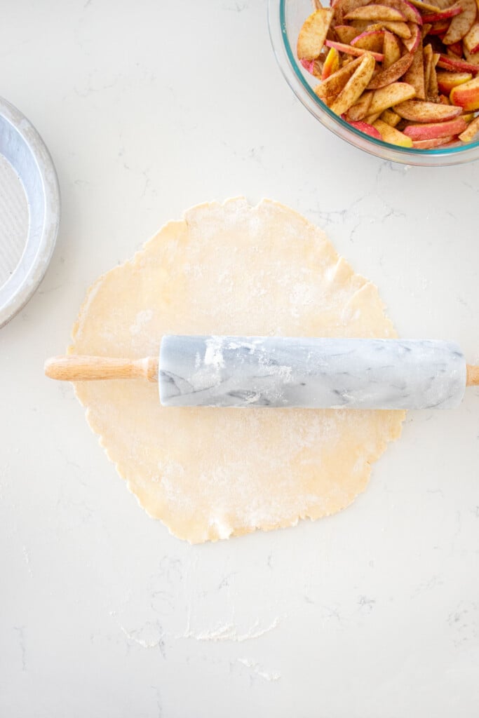 pie crust rolled out with a marble rolling pin on a marble counter.