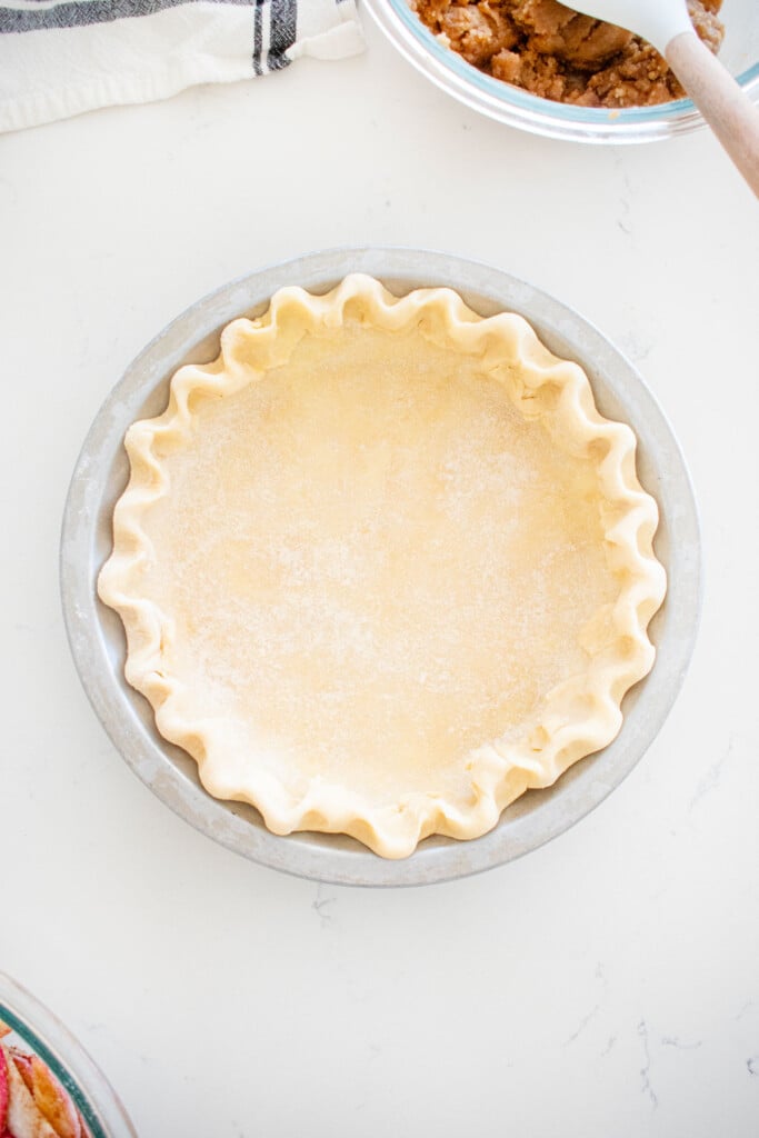 fluted pie crust in a pie pan on a marble counter.