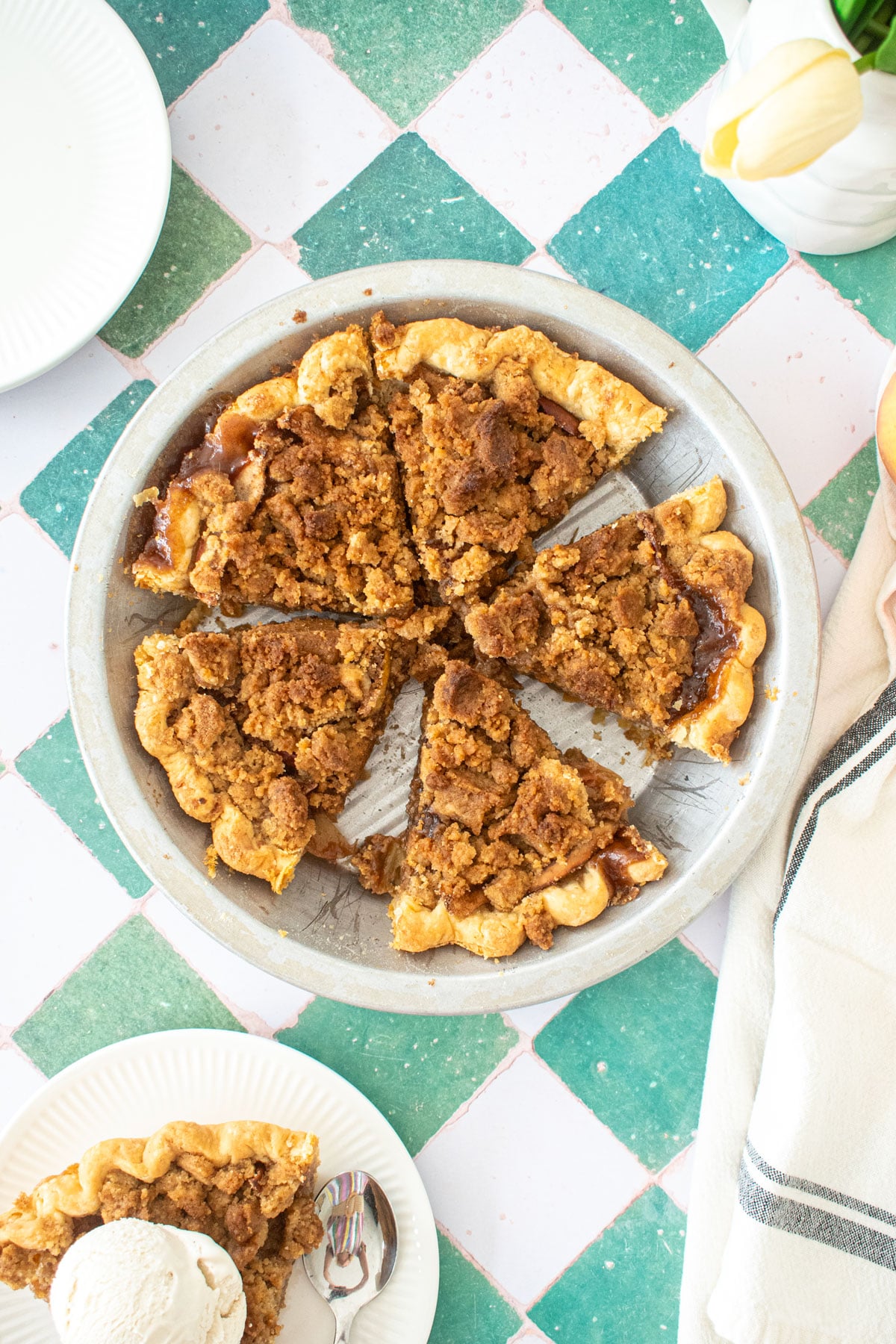 dutch apple pie cut into slices in a pie pan on a green tile table.