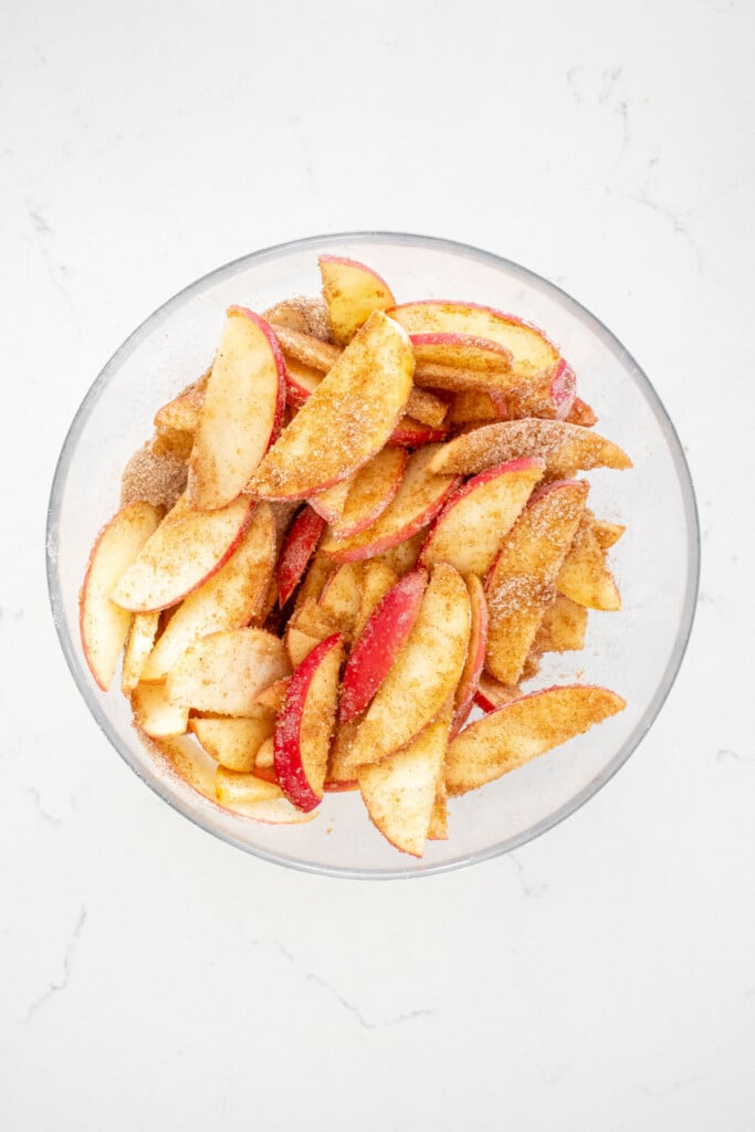 dutch apple pie filling in a glass mixing bowl on a white marble counter.