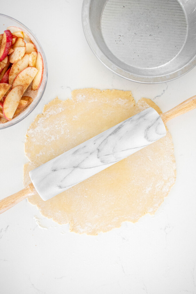 pie crust being rolled out on a white marble counter with a marble rolling pin.