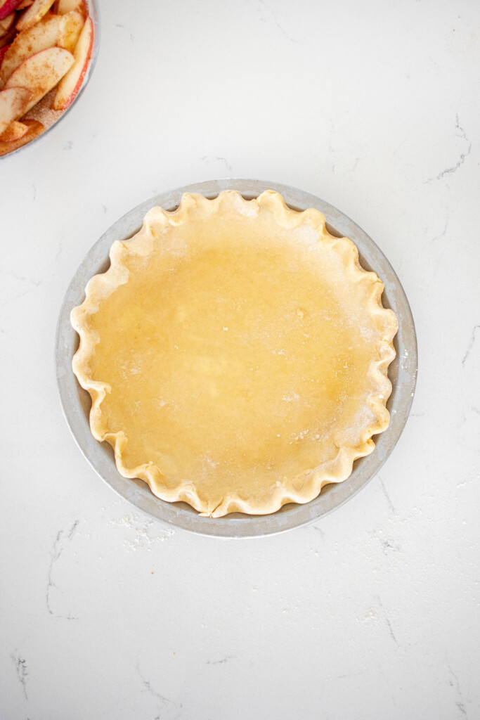 pie crust formed into a pie pan with fluted pie crust on a white marble counter.