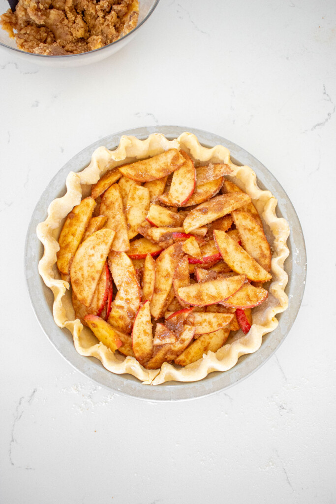 fluted pie crust with apple pie filling on a white marble counter.