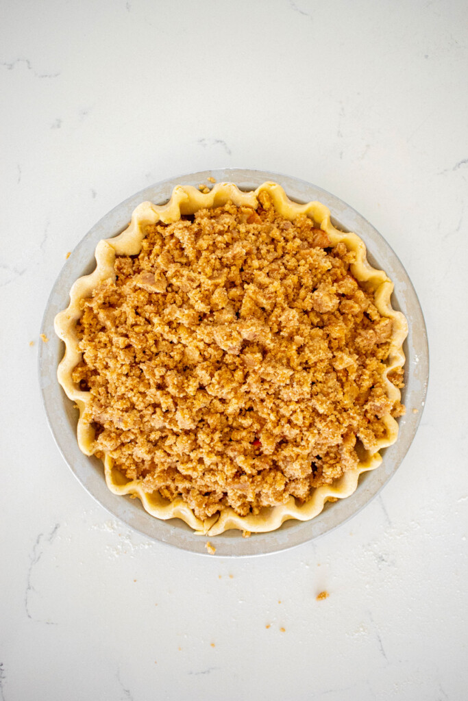 streusel filling on top of an apple pie on a white marble counter.