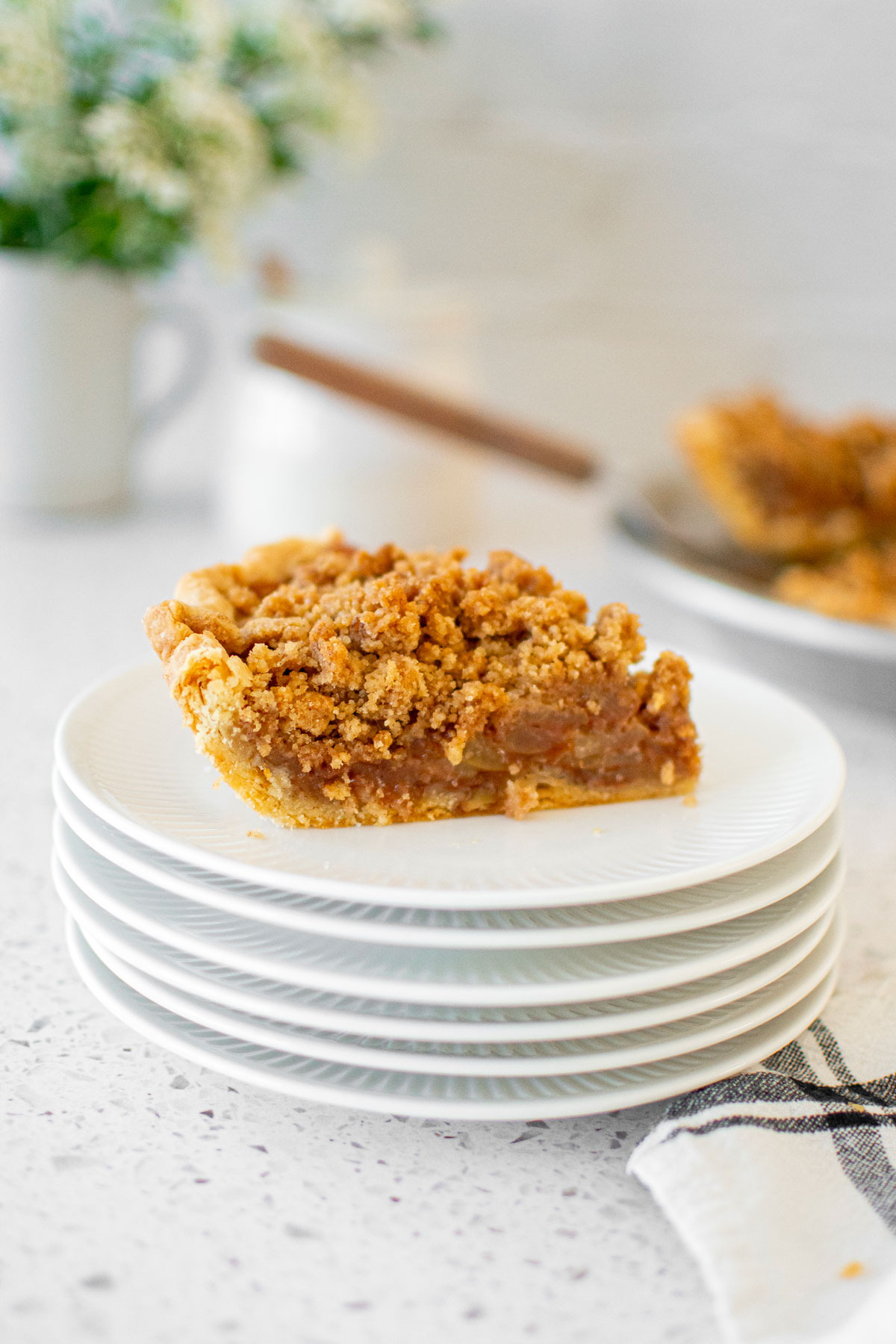 old fashioned dutch apple pie slice on a stack of white plates on a marble counter.