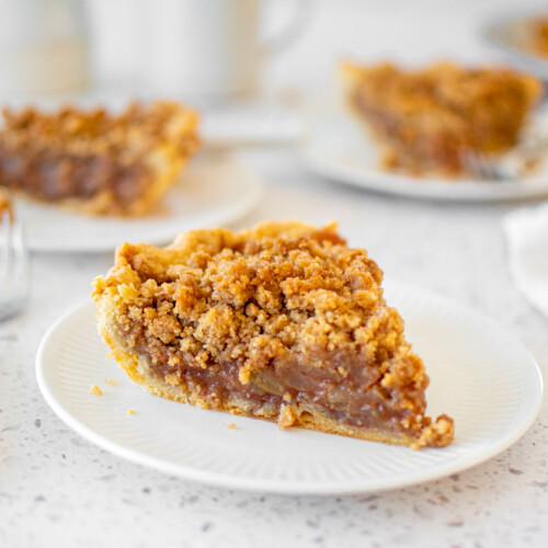 old fashioned dutch apple pie slice on a white plate on a marble counter.