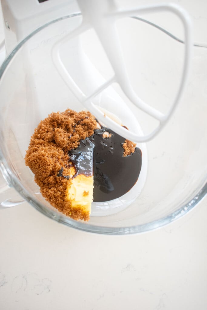 butter sugar and molasses in a glass mixing bowl on a white marble counter.