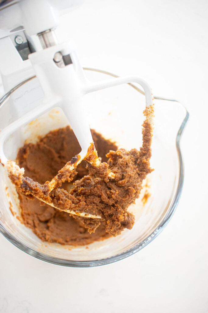 creamed butter sugar and molasses in a glass mixing bowl on a white marble counter.