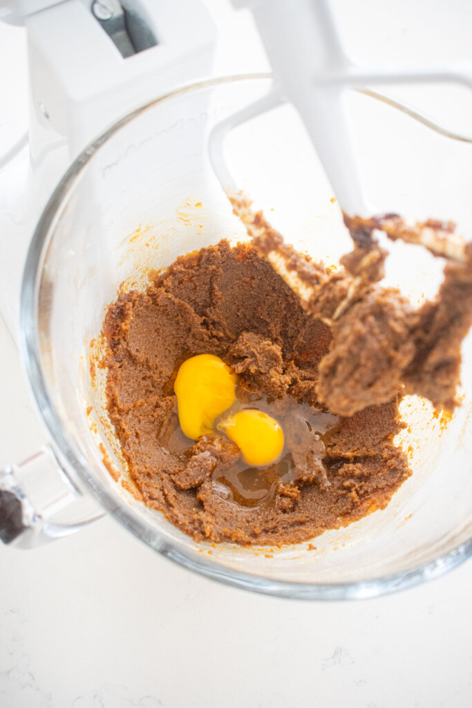 creamed butter sugar and molasses with eggs in a glass mixing bowl on a white marble counter.