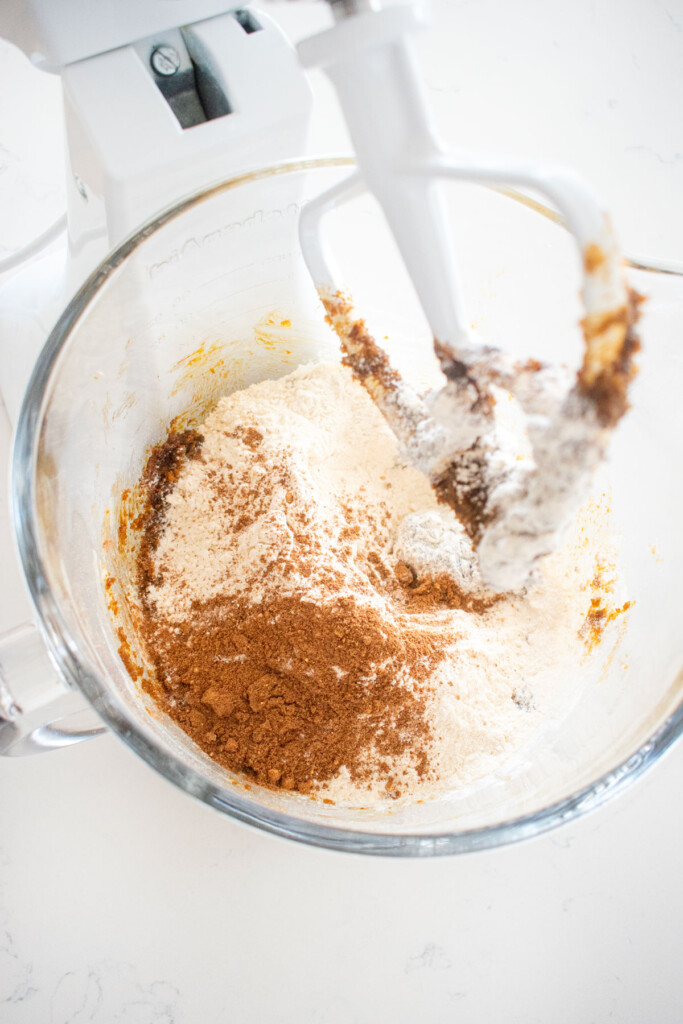 ingredients for gingerbread biscotti in a glass mixing bowl on a white marble counter.