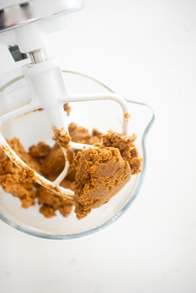gingerbread biscotti cookie dough in a glass mixing bowl on a white marble counter.