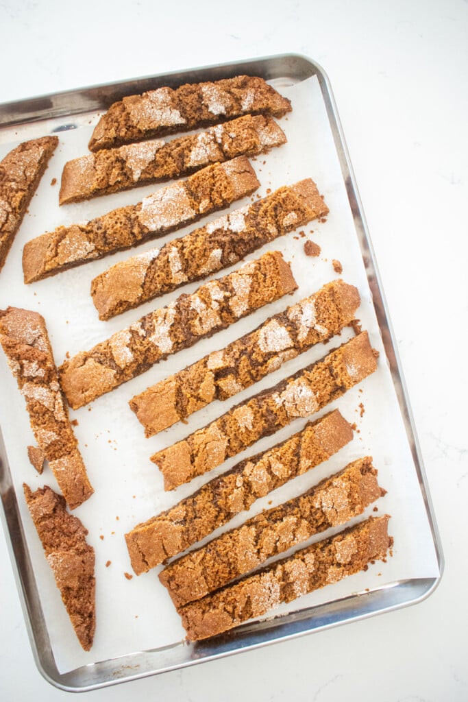 cut gingerbread biscotti on a baking sheet on a white marble counter.