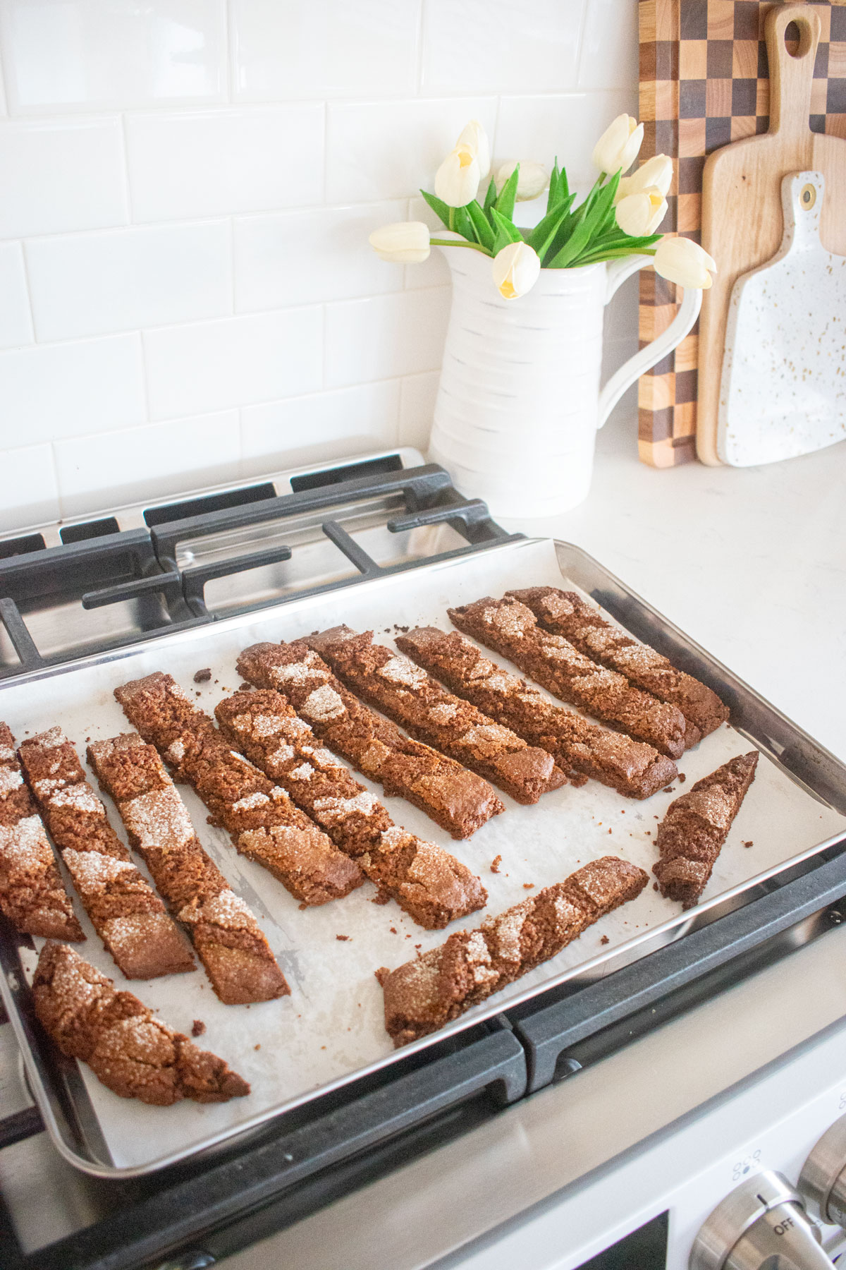 gingerbread biscotti on a baking sheet cooling on top of an oven.