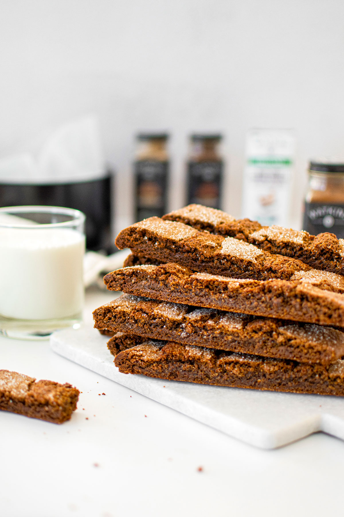 stack of gingerbread biscotti on a white marble counter with a glass of milk.