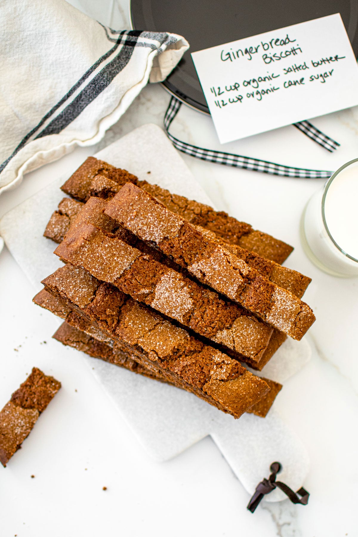 gingerbread biscotti on a white marble counter with a glass of milk.