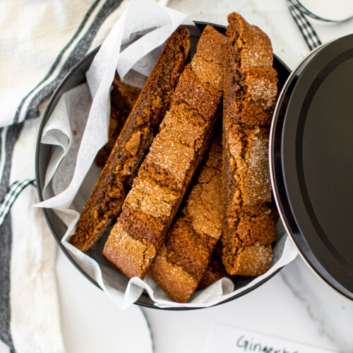 gingerbread biscotti in a tin on a white marble counter.