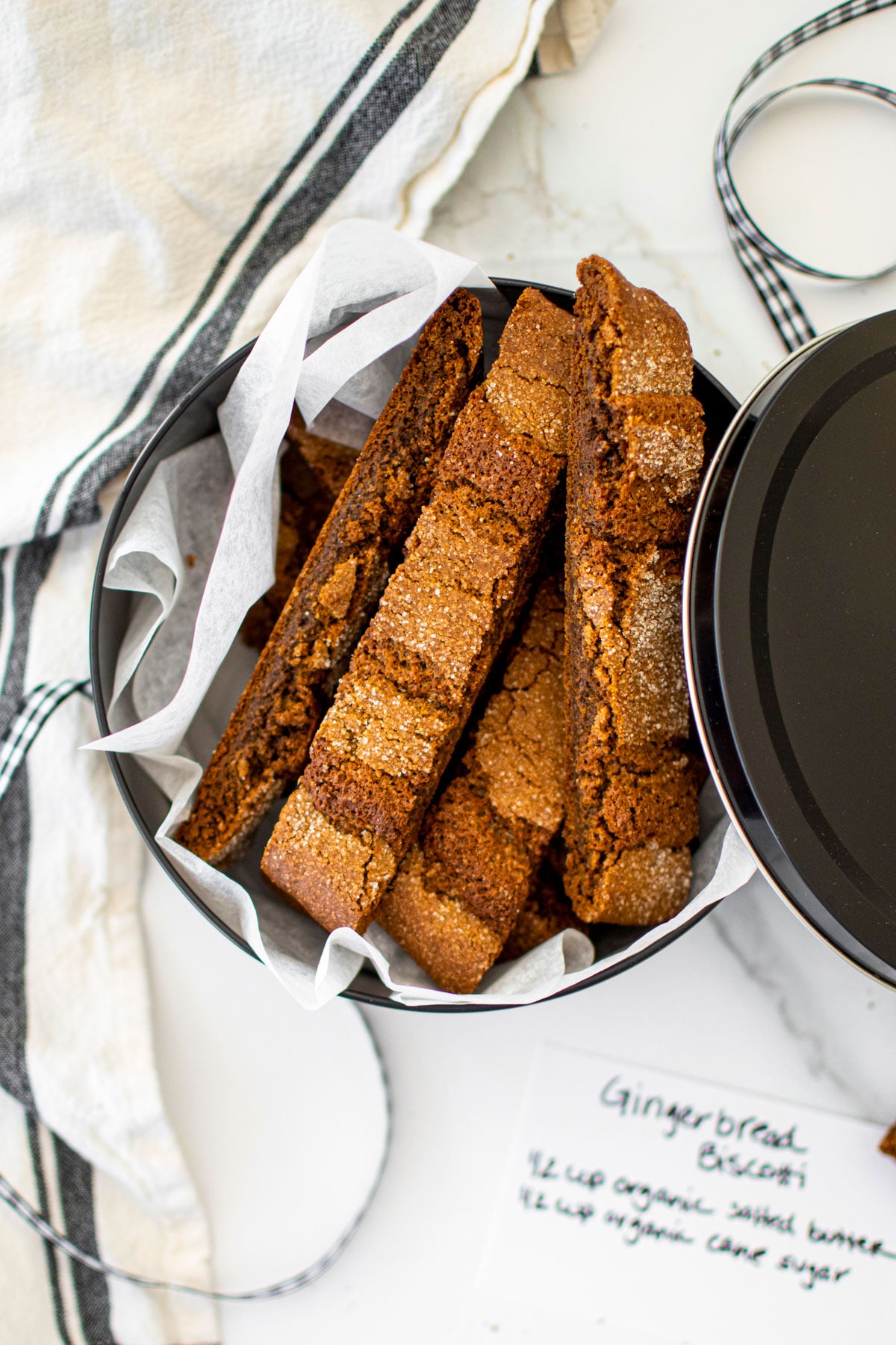 gingerbread biscotti in a tin on a white marble counter.