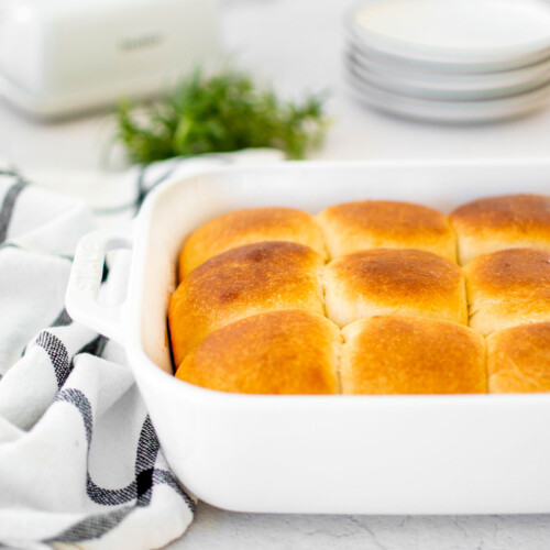 white ceramic dish of honey butter dinner rolls on the dinner table.