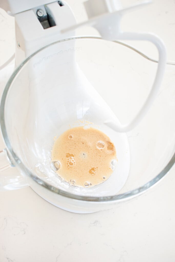 yeast and water in a glass mixing bowl on a whtie marble counter.