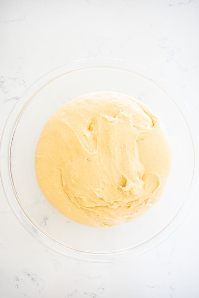 honey butter dinner rolls dough in a glass mixing bowl on a white marble counter.