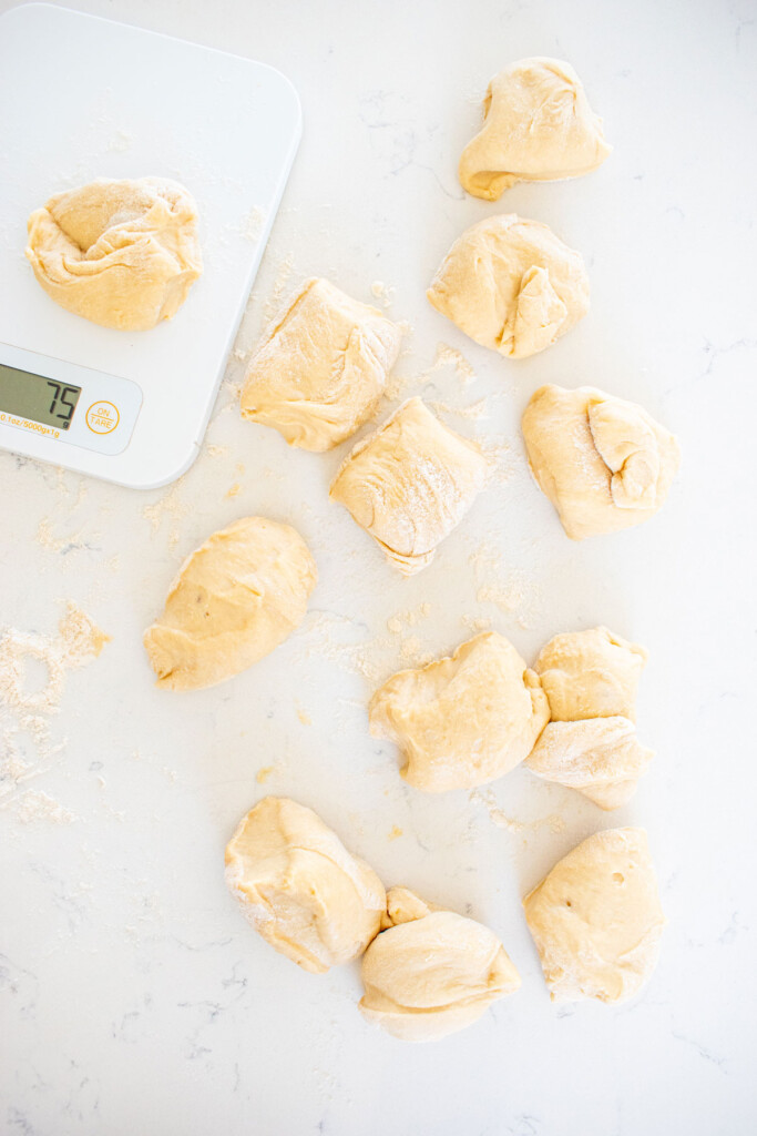 honey butter dinner rolls dough cut into pieces on a white marble counter.