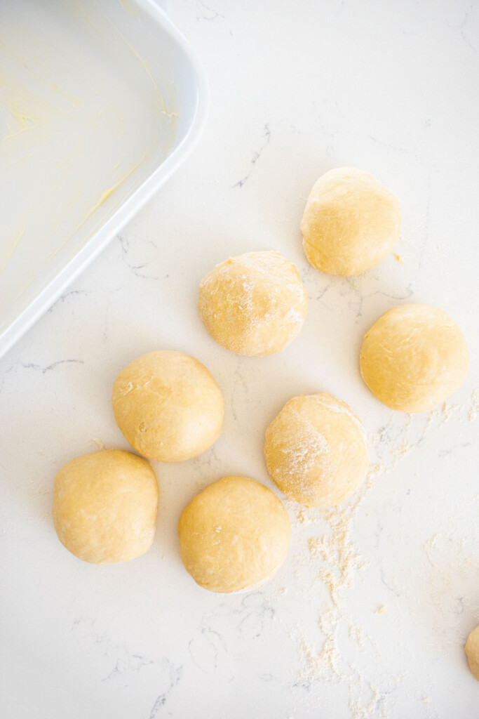 honey butter dinner rolls formed into dough balls on a marble counter.