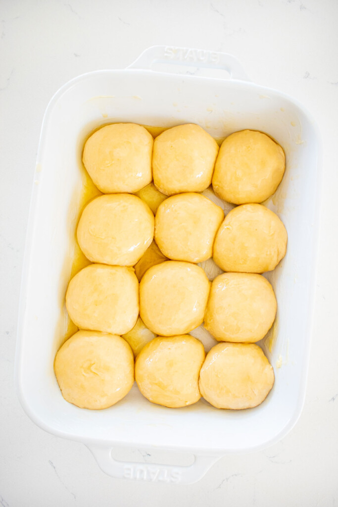 honey butter dinner rolls dough in a white ceramic baking dish on a marble counter.