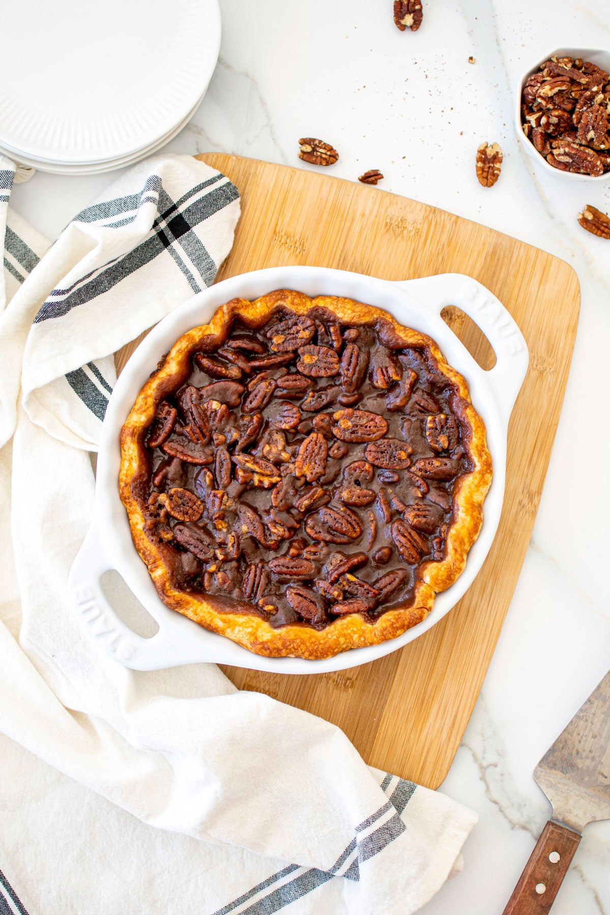 honey pecan pie in a white pie pan on a wood cutting board on a marble table.