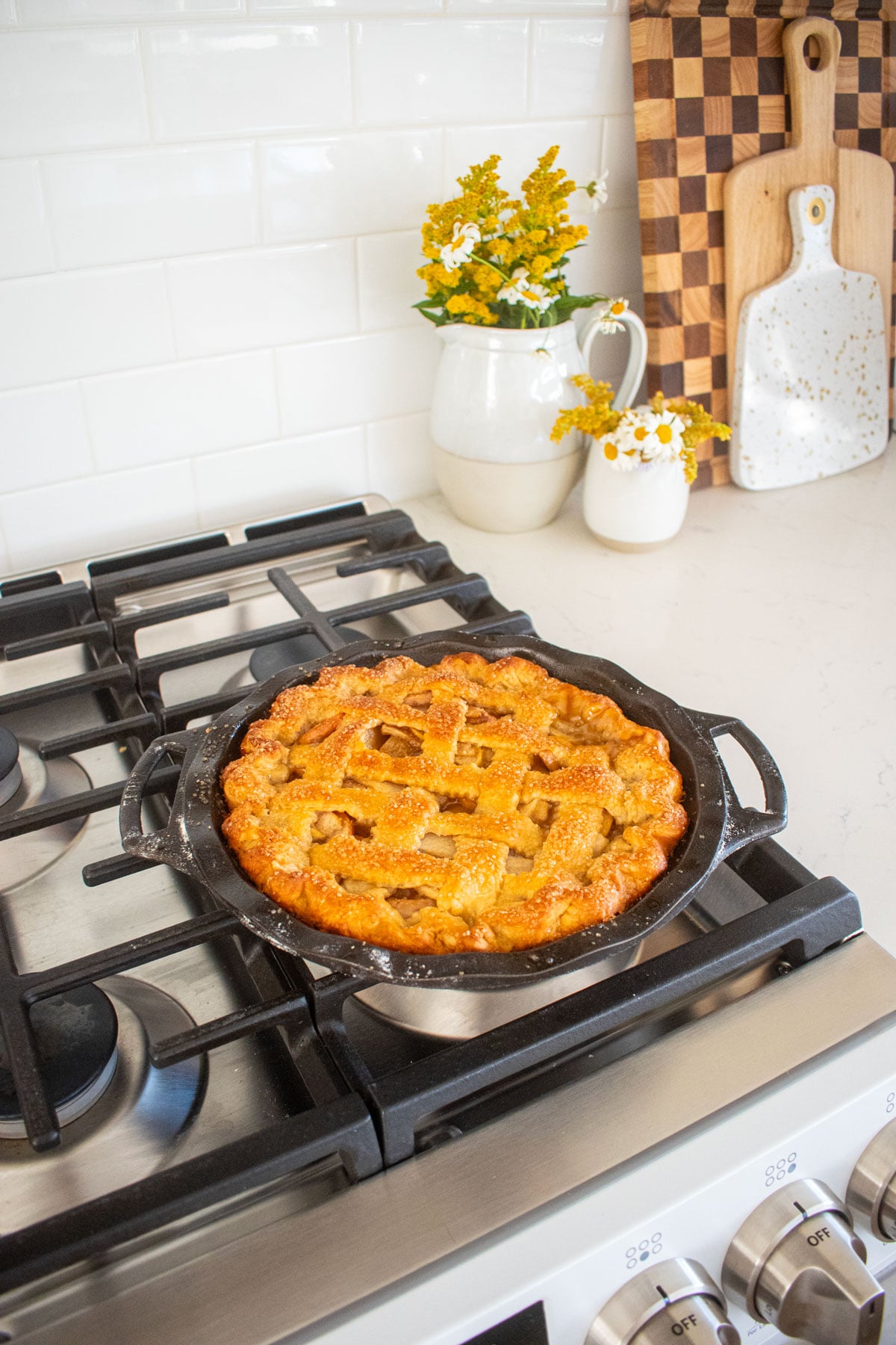 baked orange blossom honey apple pie with a lattice top and golden brown pie curst in a cast iron pie pan cooling on top of an oven.